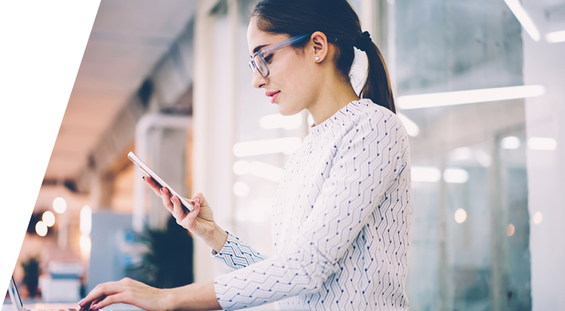 A woman checking her phone while on a laptop